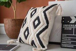 Detail of bohemian tufted throw pillow featuring black geometric patterns and corner tassels