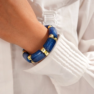 Close-up of blue sandstone stretch bracelet with gold spacers on a white shirt sleeve