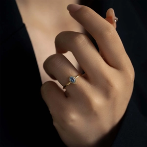 Macro shot of gold ring with a pear-shaped blue gemstone and diamond halo on a finger