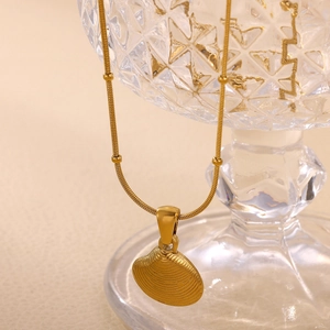 Close-up of gold shell pendant with beaded snake chain on a crystal glass rim