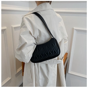 Close-up of black quilted shoulder bag with pleated texture on a model in beige coat
