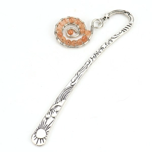 Macro view of silver bookmark with engraved celestial patterns and orange bead swirl