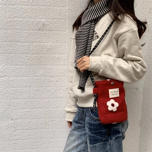 Detail of red plush crossbody bag with white 3D flower and woven strap on model