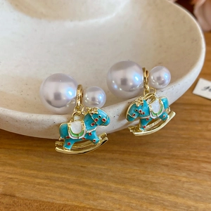 Macro shot of pearl earrings with turquoise enamel rocking horse charms on ceramic tray