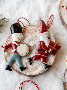 Close-up of metal drummer boy and Santa Claus ornaments on wood with faux snow