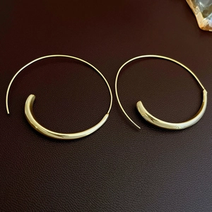 Detail of chunky gold-plated C-shape hoop earrings on dark brown leather background