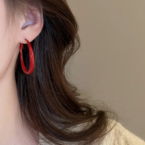 Close-up of a model wearing large red hoop earrings with a glossy minimalist finish