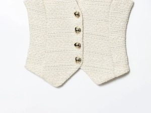 Détail du tissu en tweed texturé et des quatre boutons dorés sur un ensemble de gilet