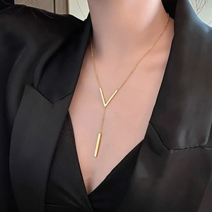 Model wearing a golden V-shaped pendant necklace with a sleek long bar on a black blazer