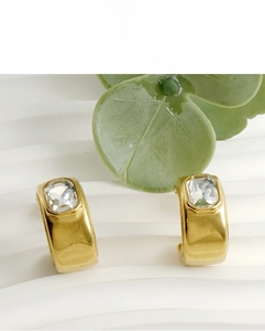 Détail de boucles d'oreilles dorées en C avec un zircon rectangulaire de taille émeraude