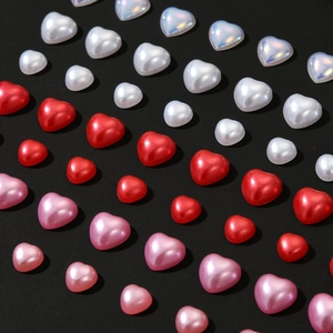 Macro shot of 3D heart-shaped pearl charms in white, red, and pink for nail art design