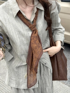 Détail d'un collier foulard en soie marron à motif cachemire sur une chemise grise