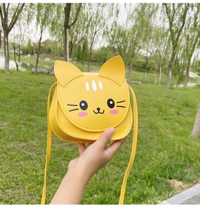Detail of yellow cat shaped PU leather crossbody bag for kids held outdoors on grass