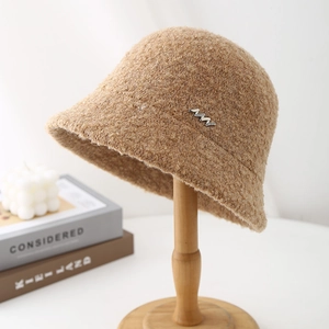 Close-up of curly boucle fabric texture and wavy silver metal badge on camel bucket hat