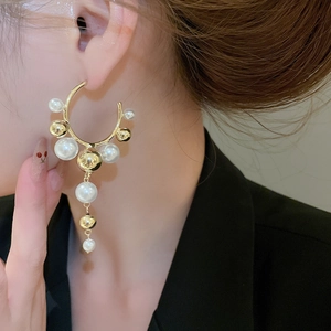 Macro detail of gold C-shaped earrings with pearls and metallic beads shown on model
