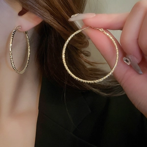Close-up of model wearing textured large gold hoop earrings with faceted metallic finish
