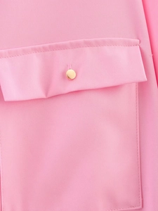 Detailed macro view of a pink shirt pocket with a shiny gold button and twill texture