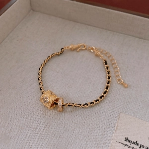 Close-up of golden woven bracelet with zircon cylinder pendant and flower charms