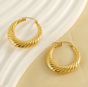 Close-up of twisted gold hoop earrings with polished spiral texture on beige silk