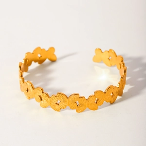 Detail showing high-polish gold plated wide open bangle with linked butterfly patterns
