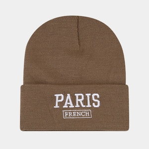 Detailed view of white PARIS FRENCH embroidery on a brown knit beanie with texture