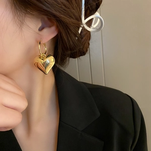 Nahaufnahme eines polierten goldenen Herzohrrings, getragen von einem Modell in Schwarz