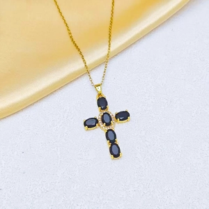 Detail of a gold cross necklace featuring oval black stones and sparkling zircon pavé