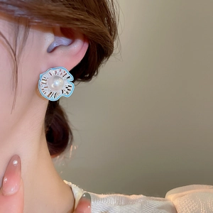 Close-up of floral pearl stud earrings with blue enamel detailing worn by a model