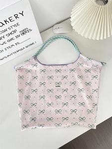 Close-up of pink tote bag with green bow print and woven rope handle on white surface