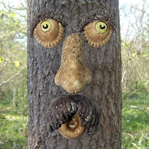 Detailed view of resin bark face ornaments installed on a tree trunk in a garden setting