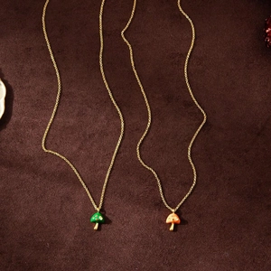 Detailed view of mushroom pendants in green and orange on golden chain necklace