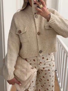 Detail of beige chunky knit cardigan with buttoned chest pockets and single-breasted closure