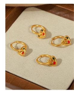 Detail of gold heart earrings with red and green enamel dots on beige fabric