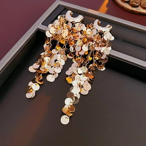 Gros plan de boucles d'oreilles dorées en U avec glands à paillettes sur plateau
