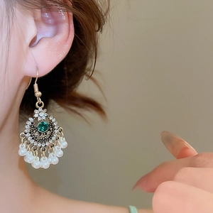 Dettaglio degli orecchini vintage dorati con gemma verde e nappe di perle bianche