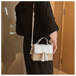 Detail of woven straw shoulder bag with white leather flap and tassel on a model