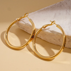 Macro detail showing CELINN lettering engraving on gold round hoop earrings