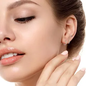Close-up of minimalist silver stainless steel hoop earrings and stud on model ear