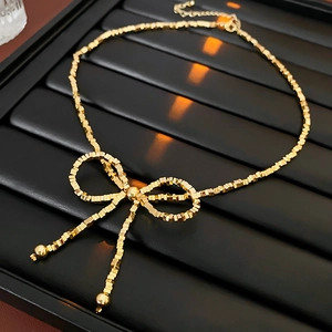 Macro detail of golden bow necklace featuring square bead chain on a dark textured background