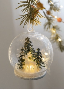 Close-up of glowing glass Christmas ball with mini pine trees and warm LED lights