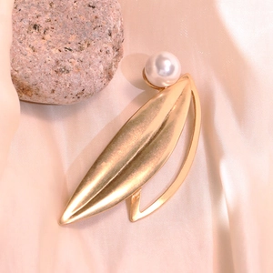 Detail of a gold leaf brooch with a white round pearl on elegant beige satin fabric
