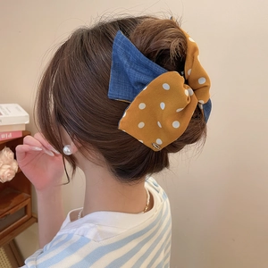 Close-up of a large yellow polka dot and blue denim bow hair clip on a model's hair