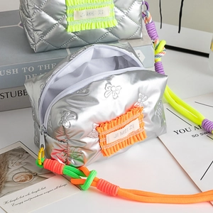 Détail d'une trousse à maquillage argentée matelassée avec texture papillon et volants