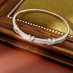 Macro detail of silver X-shaped crossover bangle with zircon pavé on green velvet