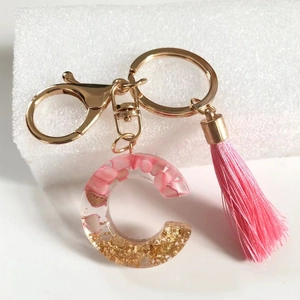 Detail of pink tassel keychain with letter C resin pendant containing gold leaf and shells