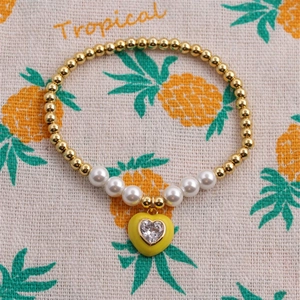 Golden beaded bracelet with white pearls and a yellow heart charm on a textured background