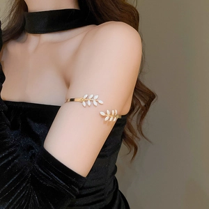 Detailed view of an adjustable golden leaf arm cuff with white enamel on a female model