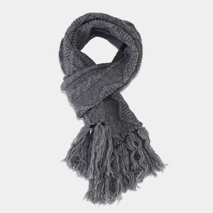 Detail of dark grey cable knit scarf featuring thick textures and decorative tassels