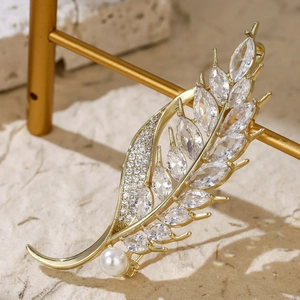 Detail of gold leaf brooch with cubic zirconia crystals and a white pearl on a display