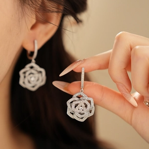 Close-up of silver hollow rose earrings with pavé zircons worn by a model in soft light